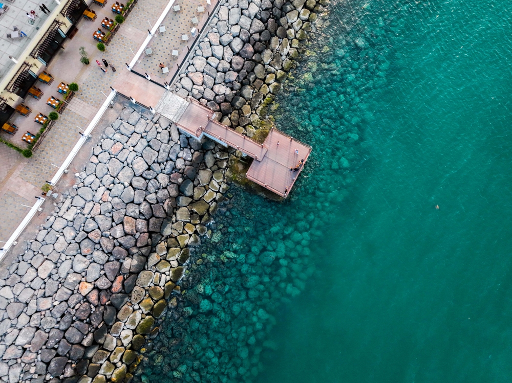 Crystal clear turquoise Arabian Gulf waters meeting stone breakwater pier at Al Marjan Island pristine coastline in Ras Al Khaimah