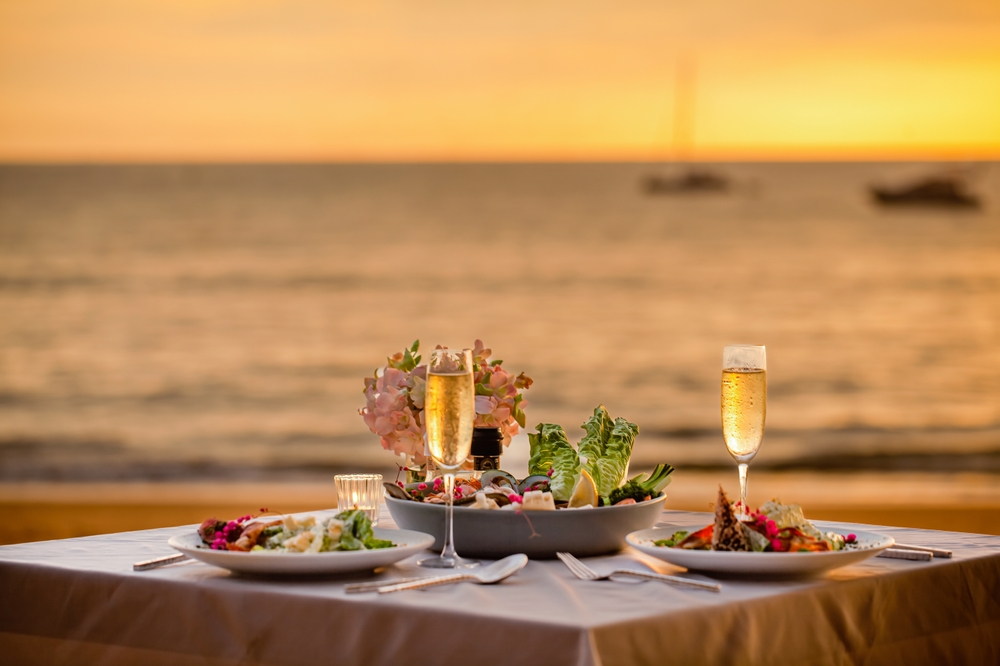 Beachfront dining experience at sunset with tables on white sand, turquoise waters, and golden sky at Al Marjan Island waterfront restaurants
